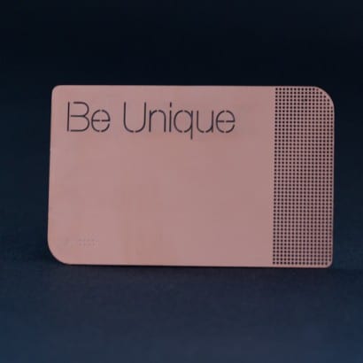 Rose gold copper metal business card with "Be Unique" text.