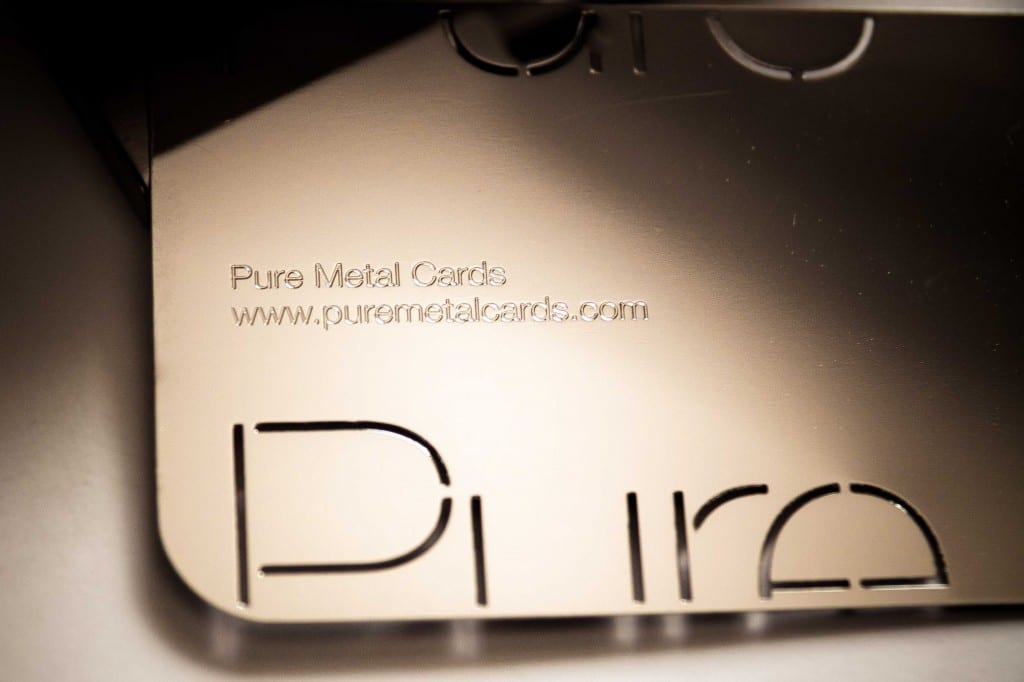 Close-up of a metallic business card with "Pure Metal Cards" and website address. The card features a cut-out design.