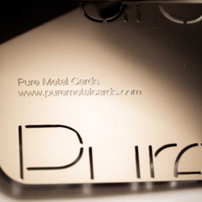 Close-up of a metallic business card with "Pure Metal Cards" and website address. The card features a cut-out design.