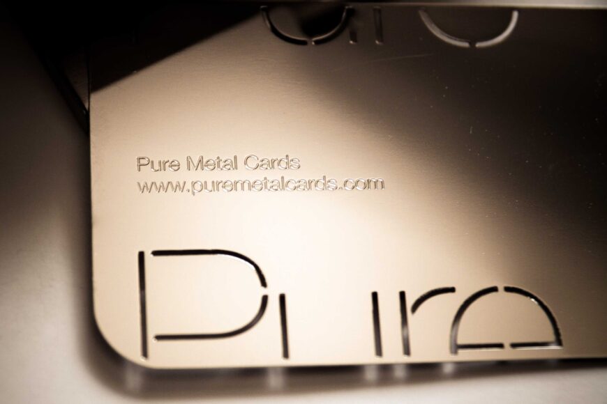 Close-up of a metallic business card with "Pure Metal Cards" and website address. The card features a cut-out design.