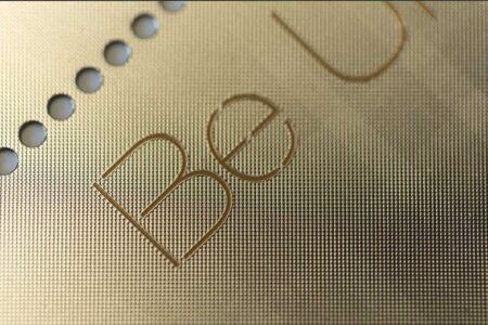 Close-up of brass prism card with "Be" engraved. Gold cards detail.