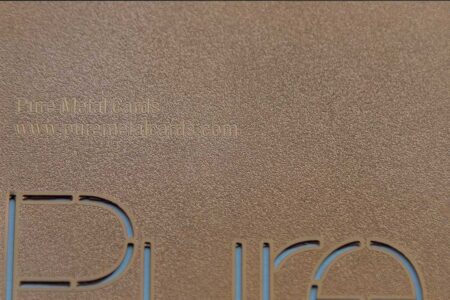 Close-up of copper frosted metal business card with "Pure Metal Cards" and website address.