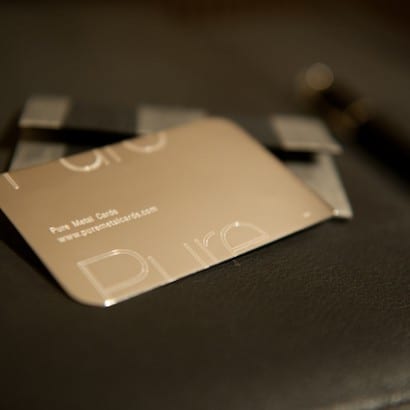 Close-up of a gold metal business card with "Pure Metal Cards" and website address. Customizable metal business cards.