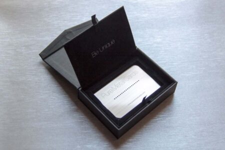 Black cardboard presentation case open, displaying a silver metal business card. "Be Unique" and "Pure Metal Cards" are visible.