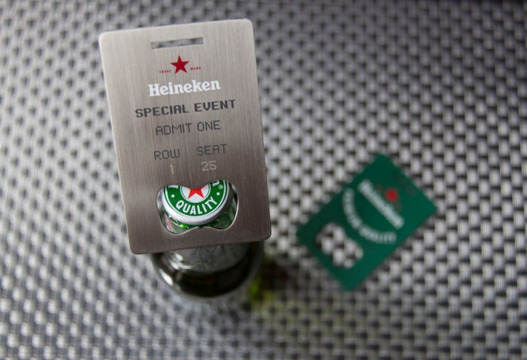 Metal Heineken bottle opener business card with "Special Event, Admit One, Row 1, Seat 25" engraved.