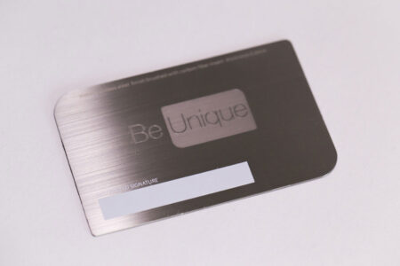 Brushed stainless steel business card with "Be Unique" and carbon fiber accents.