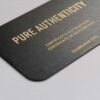 Close-up of a luxurious matt black brass card with gold lettering reading "Pure Authenticity.