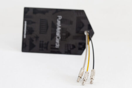 Three metal luggage tags with cables attached to a black PureMetalCards tag.