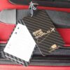 Pure-Metal-Cards-carbon-fiber-luggage-tag-20-1 Sleek carbon fiber luggage tag attached to a red suitcase. "See the World" is visible on the tag.