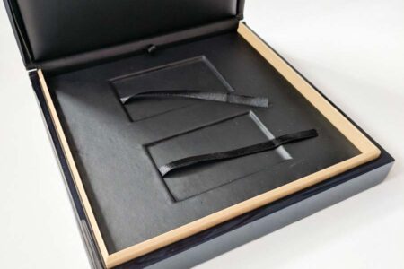 Open black luxury wood presentation case with beige interior and black ribbon inserts. "Be Unique" logo visible.