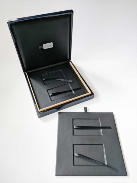Pure-Metal-Cards-luxury-wood-presentation-case_23 Open black luxury wood presentation case with compartments and black ribbons. "Be Unique" logo visible.