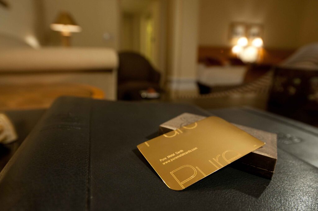 Close-up of a 24 karat gold card on a leather surface. Text: Pure Metal Cards, www.puremetalcards.com