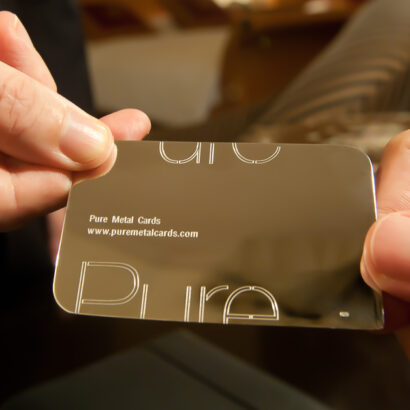 Hands holding a sleek, metallic Pure Metal Cards 18 karat gold business card. Prestige and memorable branding.