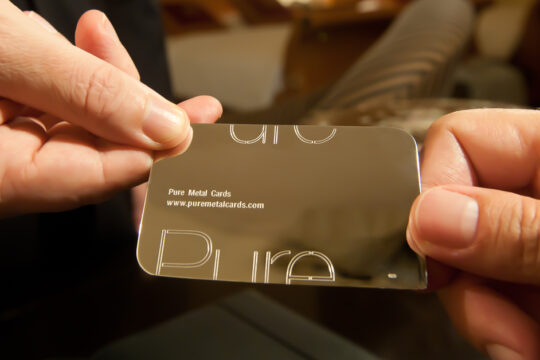 Hands holding a sleek, metallic Pure Metal Cards 18 karat gold business card. Prestige and memorable branding.