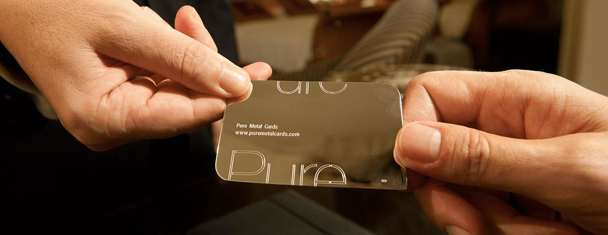 Two hands exchanging a sleek, metallic Pure Metal Cards business card.