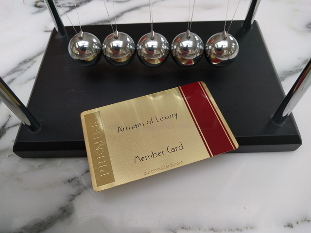 Premier Member card for Artisans of Luxury next to a Newton's cradle by puremetalcards.com