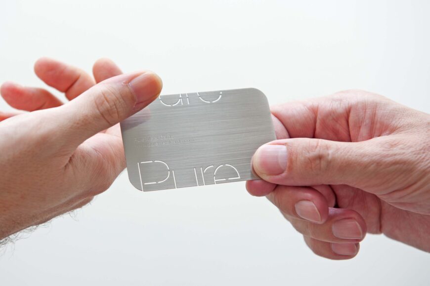 Brushed stainless steel business card held in hand, with Pure Metal Cards logo.