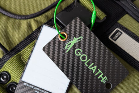 Goliath carbon fiber luggage tag attached to a green bag.