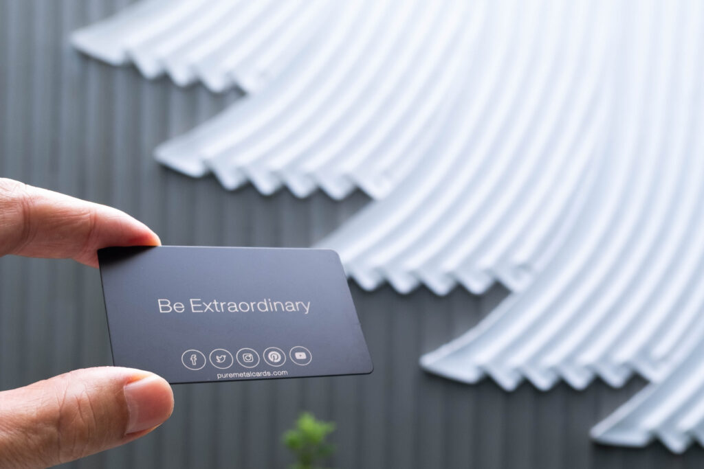 Hand holding a metal business card that says "Be Extraordinary". Pure Metal Cards. Learn more about business card size.