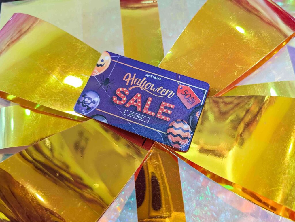 Halloween sale card on a gold background. "Halloween SALE," discount, 50% off. Premium metal card promotion.