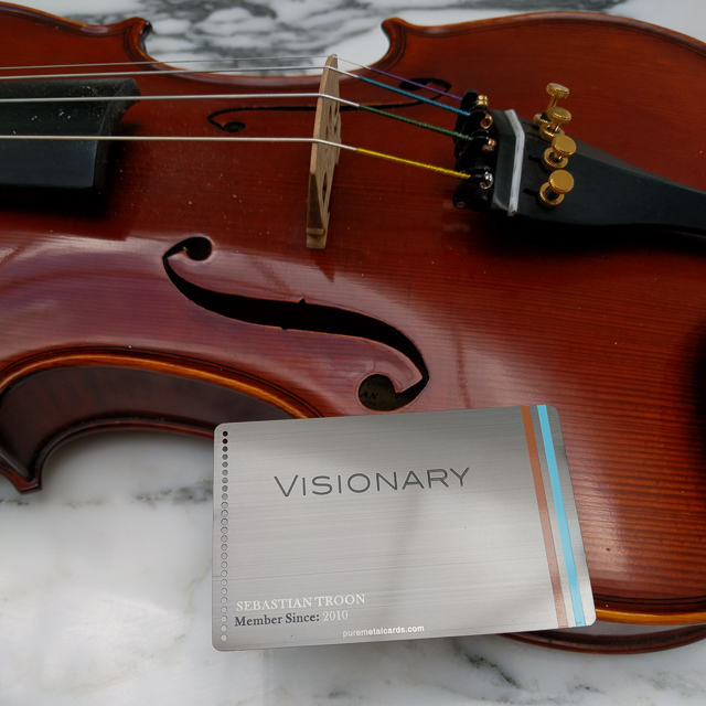 Engraved gunmetal gray metal member card with "VISIONARY" and "Sebastian Troon" on a violin by puremetalcards.com