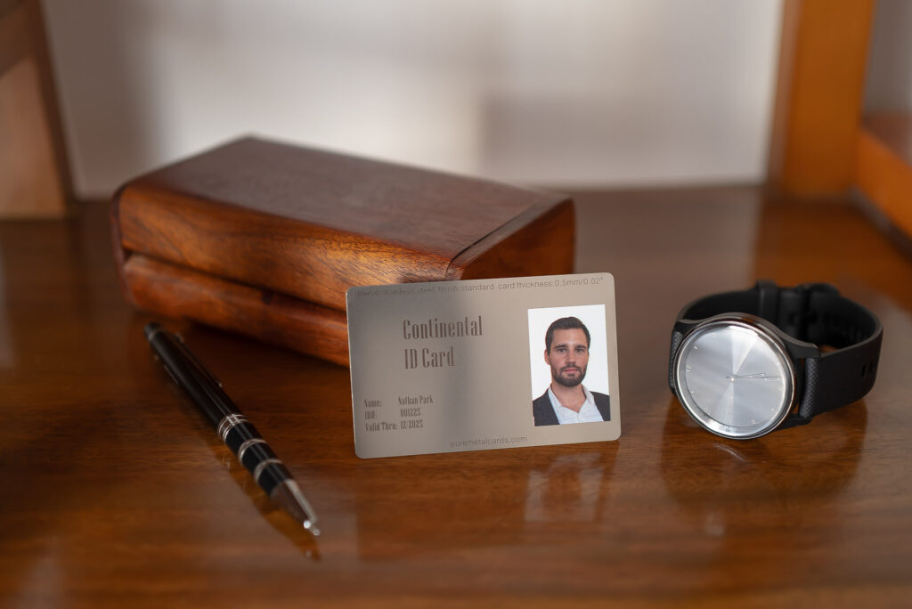 Metal badge ID card for Nathan Park with a watch and pen on a wooden desk. PureMetalCards.com