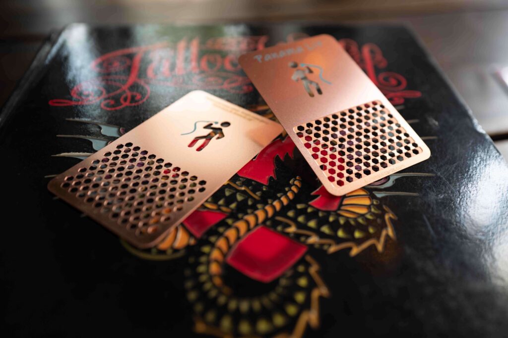 Two rose gold metal grinder cards with a honeycomb pattern, on a book with a dragon design.