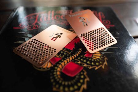 Two rose gold metal grinder cards with a honeycomb pattern, on a book with a dragon design.